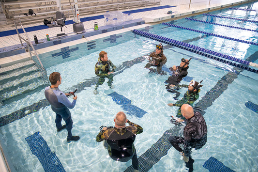 Group of six freediving students in wetsuits practicing in indoor pool pool with instructor