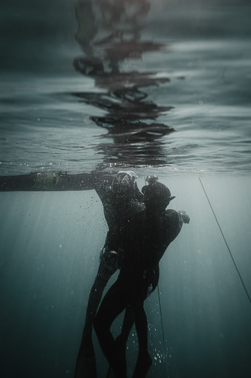 Two freedivers underwater near surface with wetsuits and fins in dark ocean water